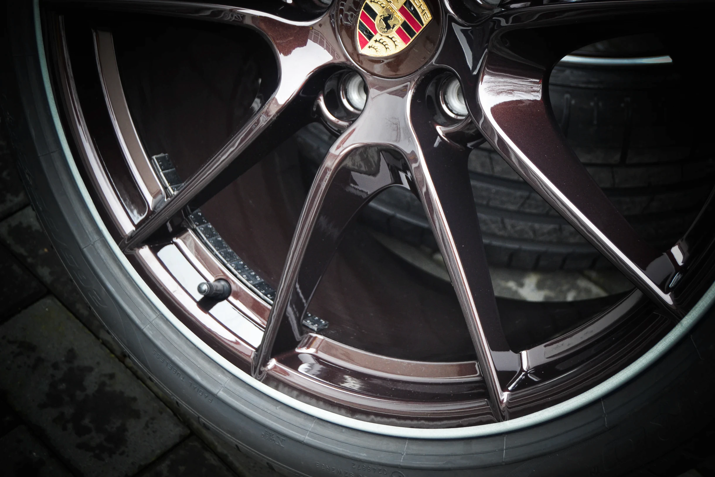 Detail der glänzenden dunklen Speichen und des Felgenrands einer Porsche-Felge bei AT Plus.
