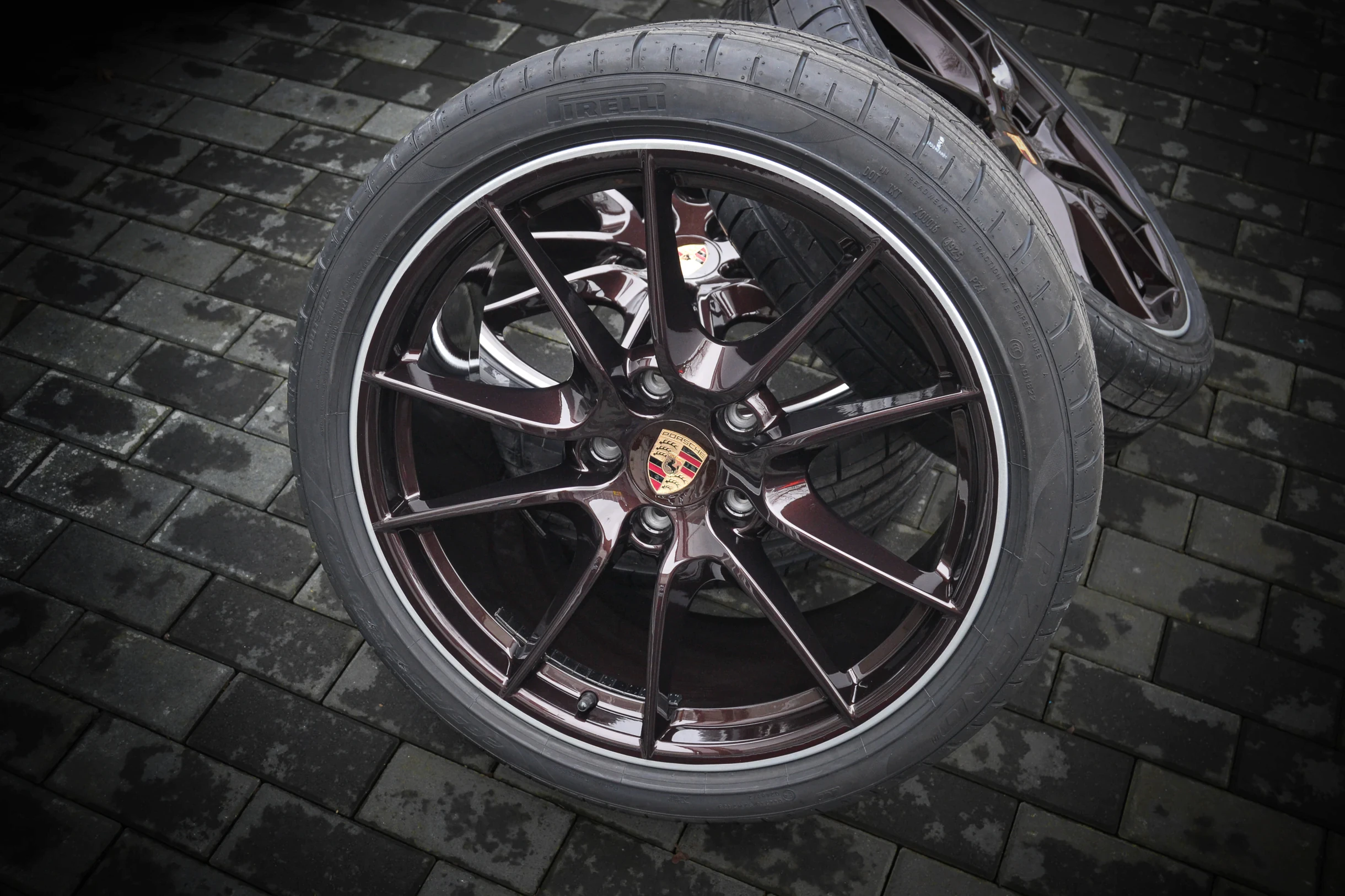 Dunkle Mehrspeichenfelge mit Porsche-Nabendeckel und montiertem Reifen, Gesamtansicht bei AT Plus.